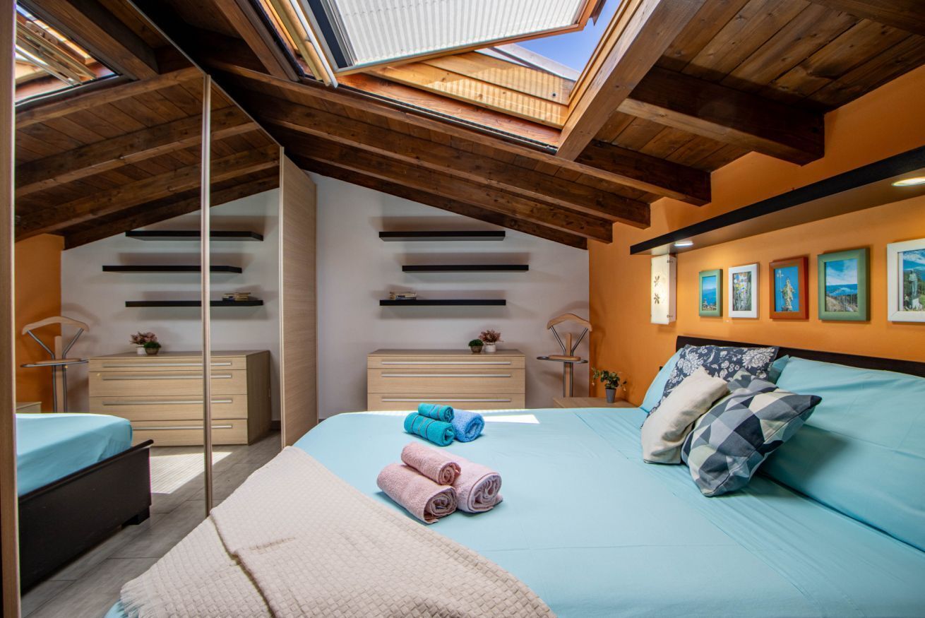 A bedroom with a skylight, a bed with rolled towels, a dresser, and artwork on the wall.