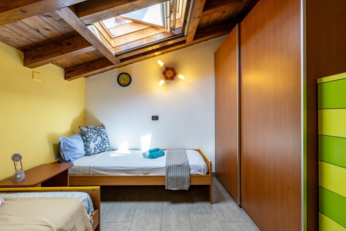 A single bed with a wooden frame, a small bedside table, a wall clock, and a skylight above.