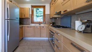 Una cocina moderna con armarios de madera, un refrigerador de acero inoxidable, una estufa a gas y una ventana con vista a un jardín.