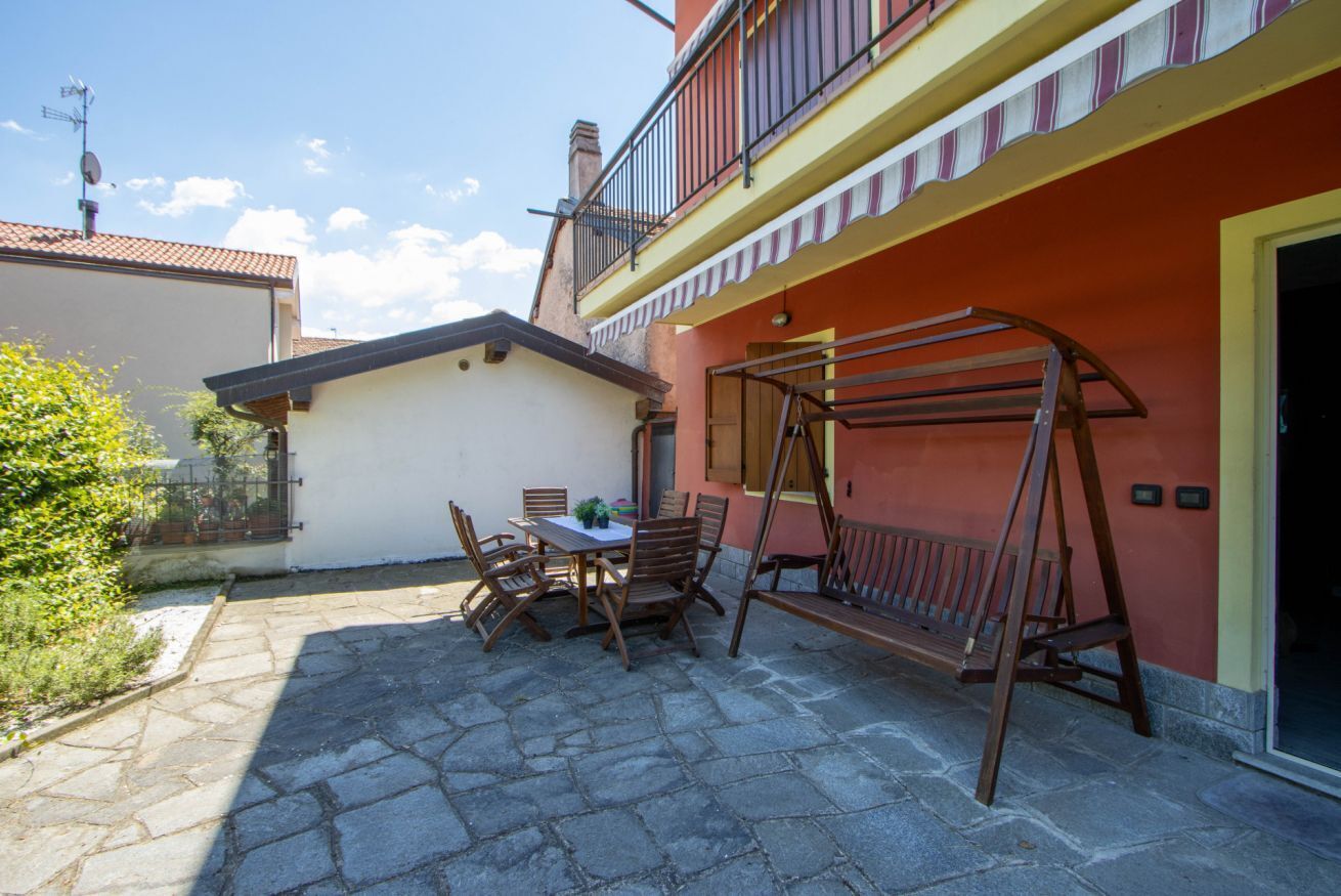Een terras buiten met een tafel en stoelen, een houten schommel en een rood gebouw met een balkon.