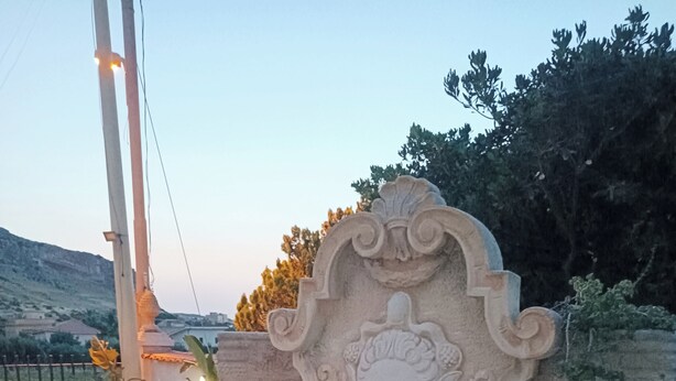 A stone fountain with a decorative head, surrounded by potted plants and a seating area. - Villa Rosalia with Heated Private Jacuzzi & Sunset View (Tonnara di Bonagia VALDERICE)