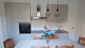 A modern kitchen with a dining table, chairs, and a vase with flowers. - Villa Rosalia with Heated Private Jacuzzi & Sunset View (Tonnara di Bonagia VALDERICE)