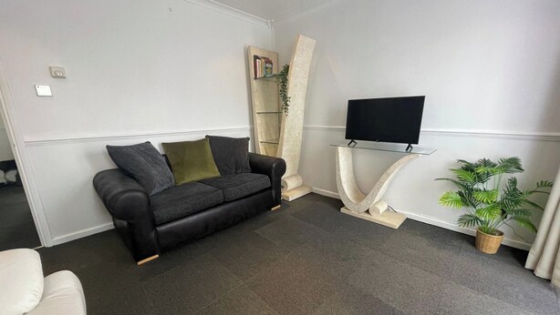 A living room with a black sofa, a flat-screen TV on a stand, a potted plant, and a bookshelf. - One Bedroom Apartment Sleeps 2 With Free Parking (London)