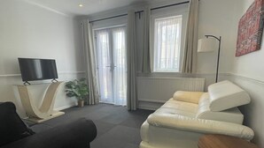A living room with a sofa, a television on a stand, a potted plant, and a lamp. - One Bedroom Apartment Sleeps 2 With Free Parking (London)