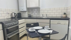 A compact kitchen with a Bosch dishwasher, a stove, and a sink. There is a dining table with plates and a cup, and a chair. - One Bedroom Apartment Sleeps 2 With Free Parking (London)