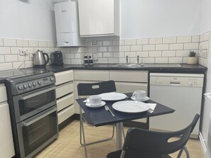 A compact kitchen with a Bosch dishwasher, a stove, and a sink. There is a dining table with plates and a cup, and a chair. - One Bedroom Apartment Sleeps 2 With Free Parking (London)