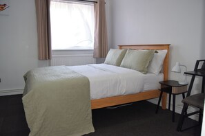 A bedroom with a single bed, a bedside table, a chair, and a window with curtains. - One Bedroom Apartment Sleeps 2 With Free Parking (London)