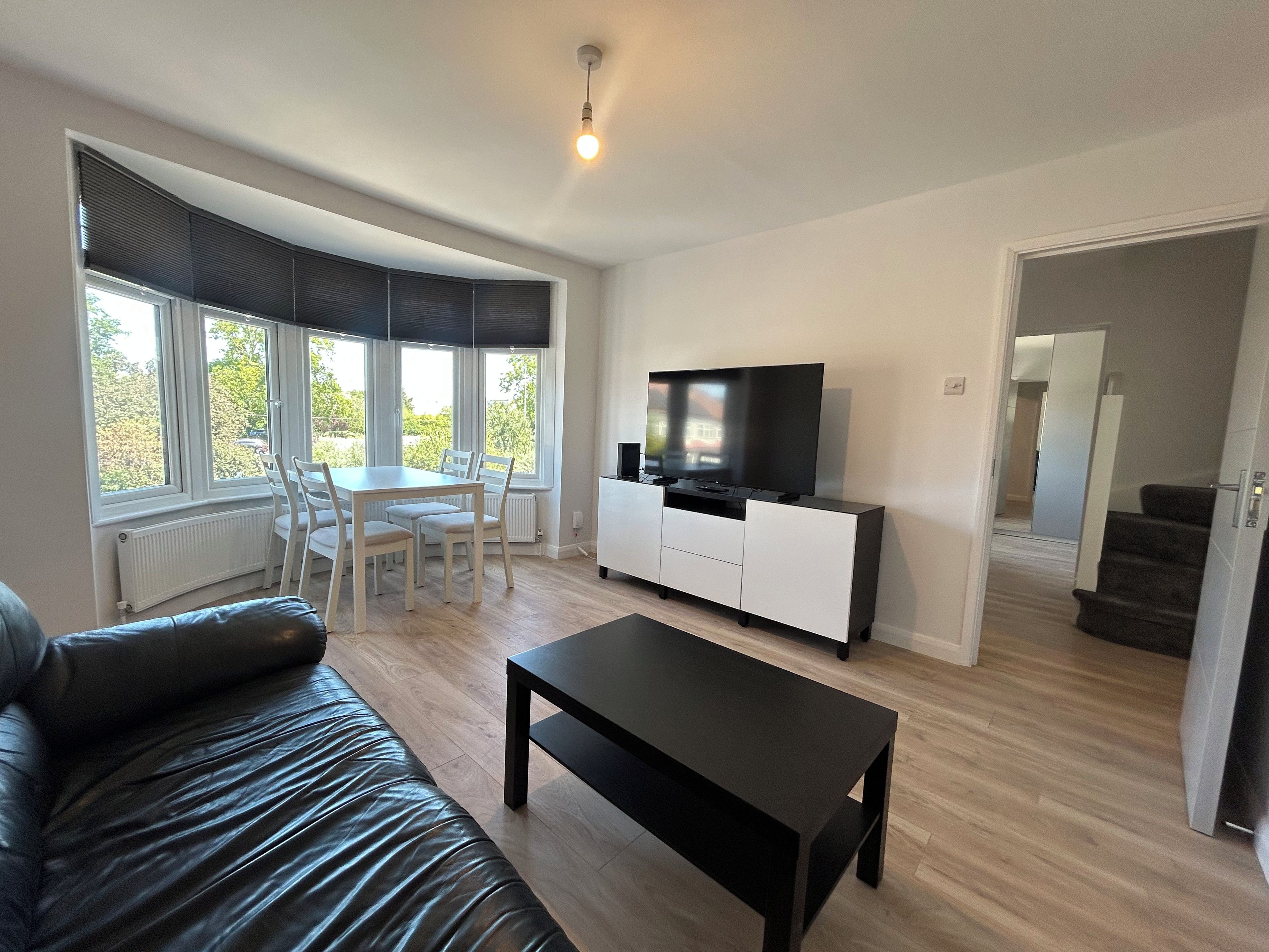A modern living room with a sofa, a coffee table, a TV on a cabinet, and a dining area with chairs and a table.