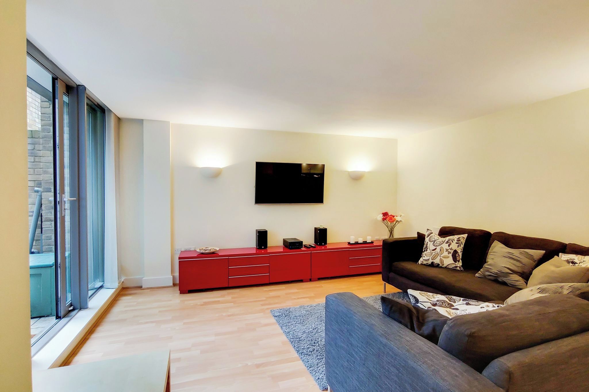 Una sala moderna con un televisor grande, un mueble de entretenimiento rojo y un sofá marrón.