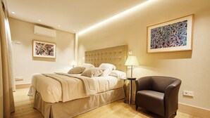 A hotel room with a bed, bedside tables, a chair, and artwork on the walls. - Nexus Santa María Luxury Apartments (VALLADOLID)