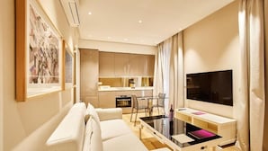 A modern living room with a sofa, a TV, a dining table, and a kitchen in the background. - Nexus Santa María Luxury Apartments (VALLADOLID)