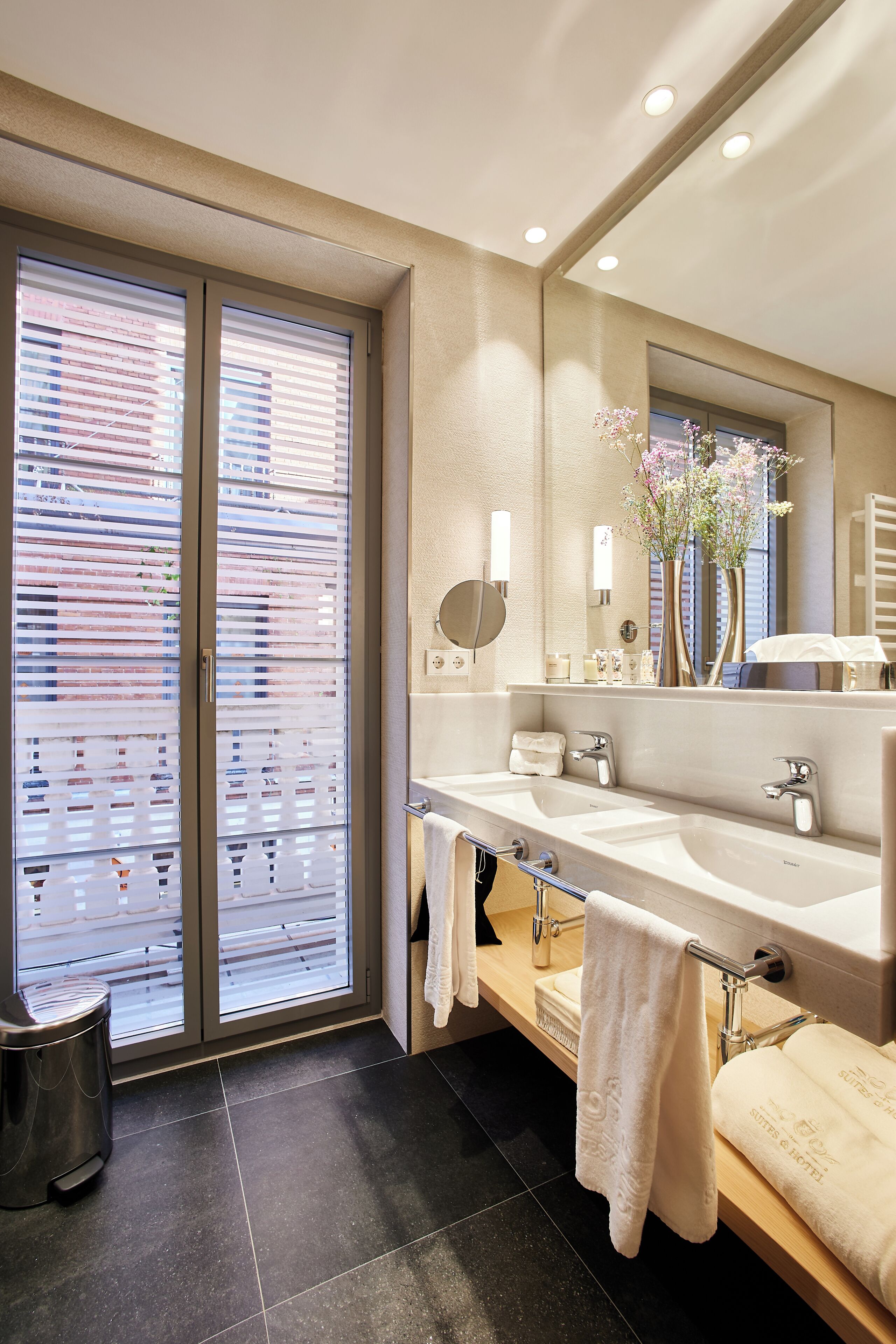 A modern bathroom with a double sink, a large mirror, and a view of a building through the window.