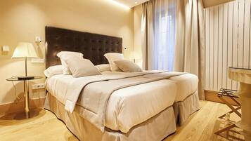 A hotel room with a large bed, two bedside lamps, a bedside table, and a window with curtains.