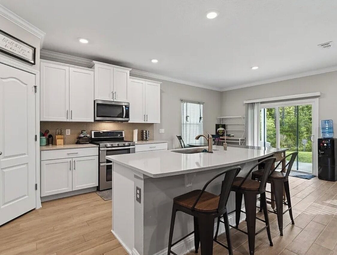 A modern kitchen with white cabinetry, a central island with bar stools, a microwave, and a stove.