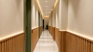 A corridor with wooden paneling on the walls and a marble floor, leading to a door at the end.