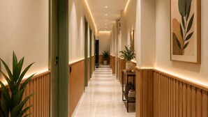 Un pasillo de hotel con paneles de madera, suelo de mármol, iluminación empotrada y cuadros en las paredes.