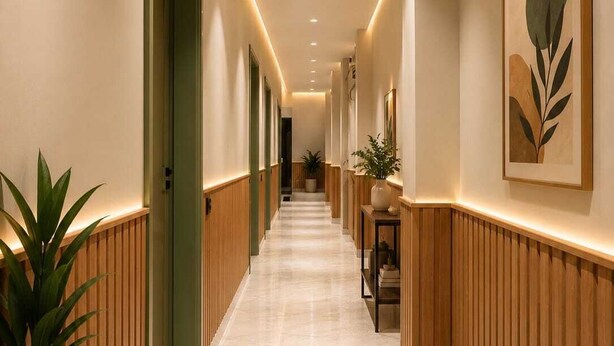 A hotel corridor with wooden paneling, marble flooring, recessed lighting, and framed artwork on the walls.