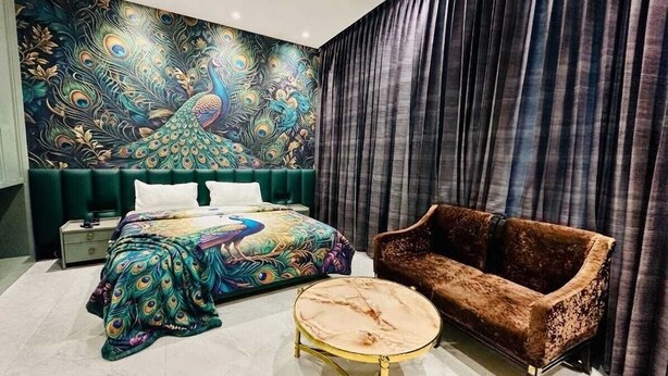 Un dormitorio con cama, sofá, una mesa de centro redonda y un mural en la pared con motivos de pavo real.