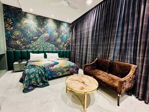 Une chambre à coucher comprenant un lit, un canapé, une table basse ronde et une fresque murale sur le thème du paon.
