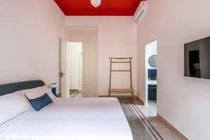 A bedroom with a bed, a wooden chair, a mirror, and a TV on the wall. - Roma 1923 - Casa Blu by Wonderful Italy (Palermo)
