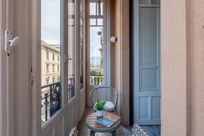 A balcony with a wicker chair, a small table with a plant and a book, and a view of buildings. - Roma 1923 - Casa Verde by Wonderful Italy (Palermo)