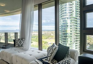 Ein modernes Wohnzimmer mit einem großen Fenster, einem weißen Sofa und Blick auf einen Wolkenkratzer.
