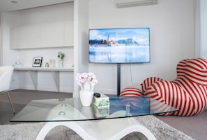 A modern living room with a glass coffee table, a flat-screen TV mounted on the wall, and a red-striped sofa. - Skyline Serenity @ Olympic Park (Sydney Olympic Park)