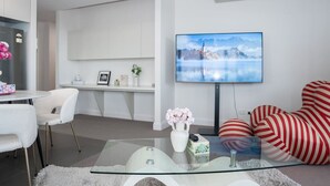 Ein modernes Wohnzimmer mit Glastisch, Flachbildfernseher, einer Couch und einem Schreibtisch.