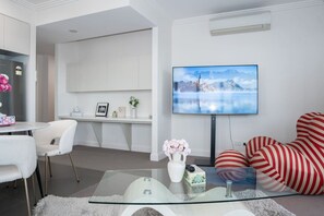 Ein modernes Wohnzimmer mit Glastisch, Flachbildfernseher, einer Couch und einem Schreibtisch.