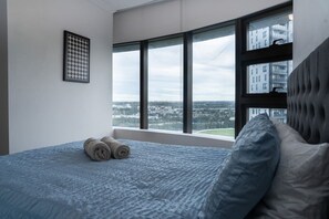Ein Schlafzimmer mit großem Fenster, einem Bett mit aufgerollten Handtüchern und Blick auf die Stadt.