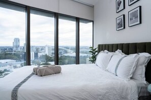 A hotel room with a large bed, a view of the city, and framed pictures on the wall. - Skyline Serenity @ Olympic Park (Sydney Olympic Park)