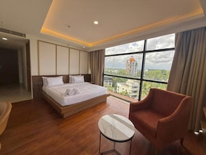A hotel room with a bed, a round table, and a view of buildings through large windows.