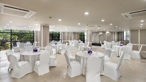 A spacious indoor venue with multiple round tables and white chairs, large windows, and a modern ceiling design. - Hotel Explora Calicut by Nova (Kozhikode)