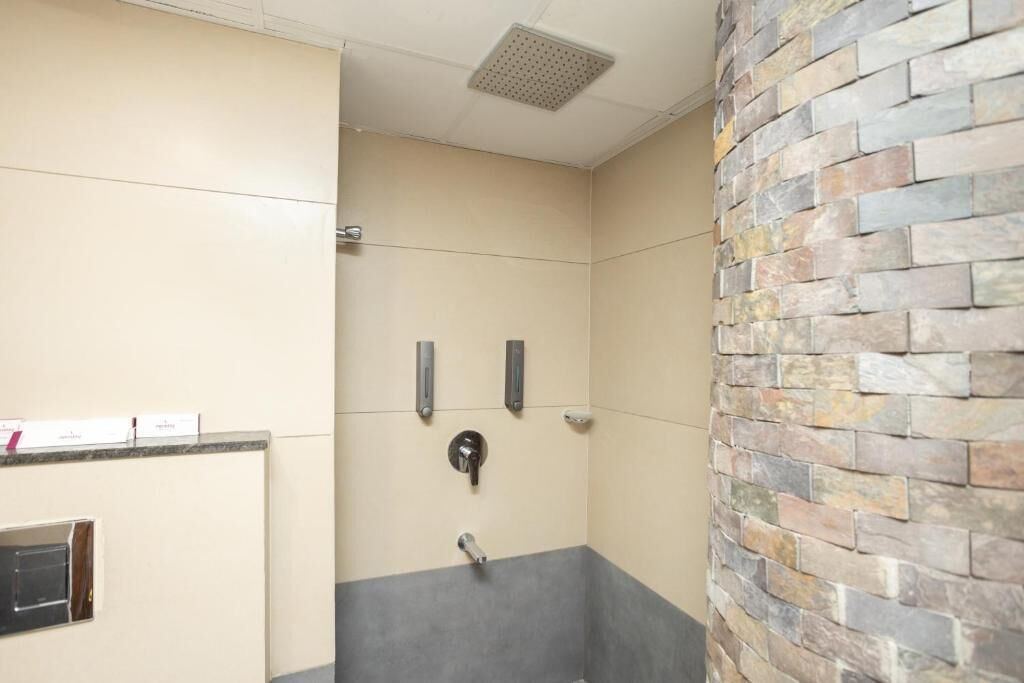 A bathroom with a beige and gray wall, a stone accent wall, and a shower area with a control panel.