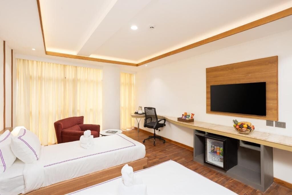 A hotel room with two beds, a desk, a chair, a television, and a minibar.