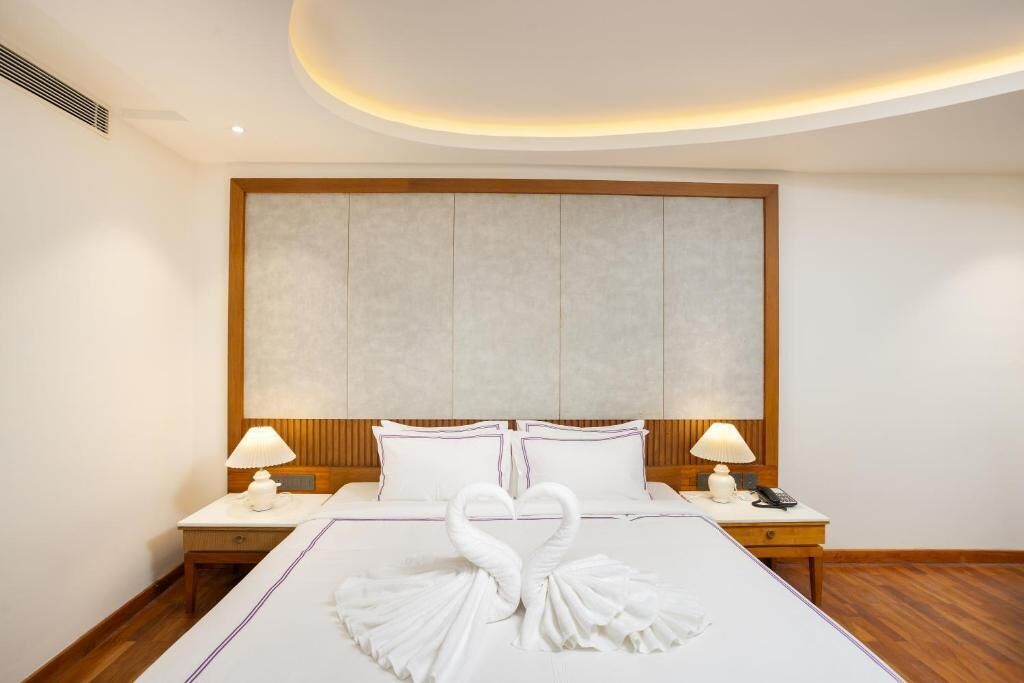 A hotel room with a large bed, two bedside lamps, a wooden headboard, and a swan-shaped towel decoration.