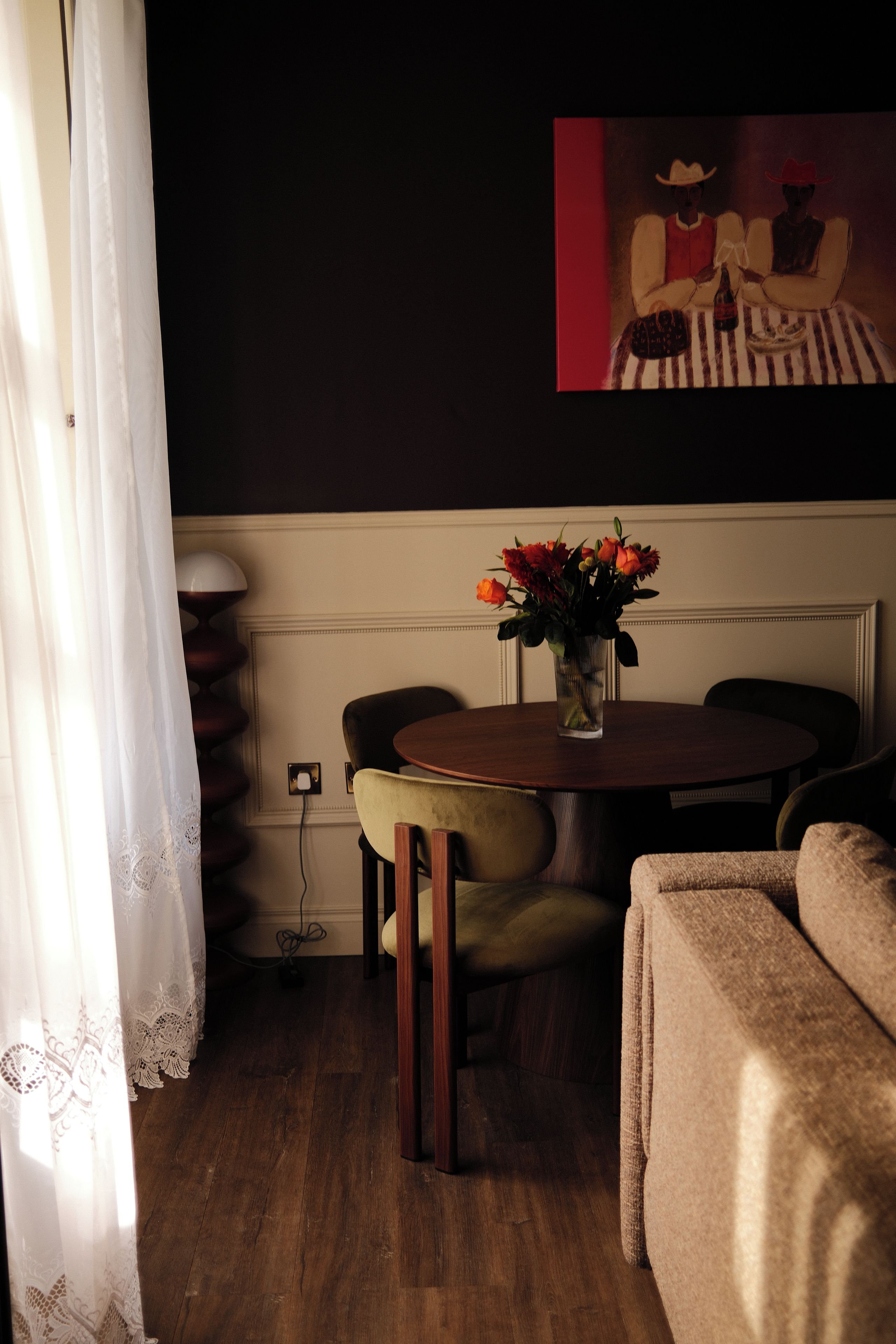 A dining area with a table, chairs, a vase with flowers, and a painting on the wall.