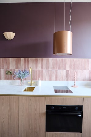 A modern kitchen with a white countertop, a stainless steel sink, a gold faucet, and a black dishwasher.