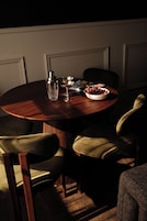 A round wooden table with a bottle, a glass, and a bowl of grapes.