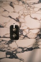 A bathroom with a marble floor and a black, metallic object, possibly a towel warmer or a heater, on the wall.