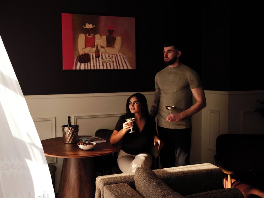 A room with a round table, a sofa, a painting on the wall, and a person standing.
