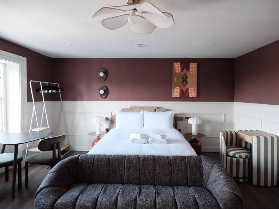 Quarto de hotel com cama, área de estar, escrivaninha e ventilador de teto.