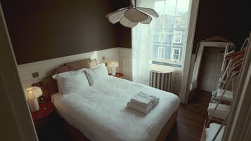 Habitación de hotel con una cama grande, lámparas de noche, vistas de la ciudad a través de la ventana y una puerta que da a un pasillo con un tendedero.