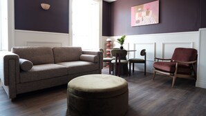 A living room with a sofa, ottoman, chairs, and a painting on the wall. - Meus Apartments (Edinburgh)
