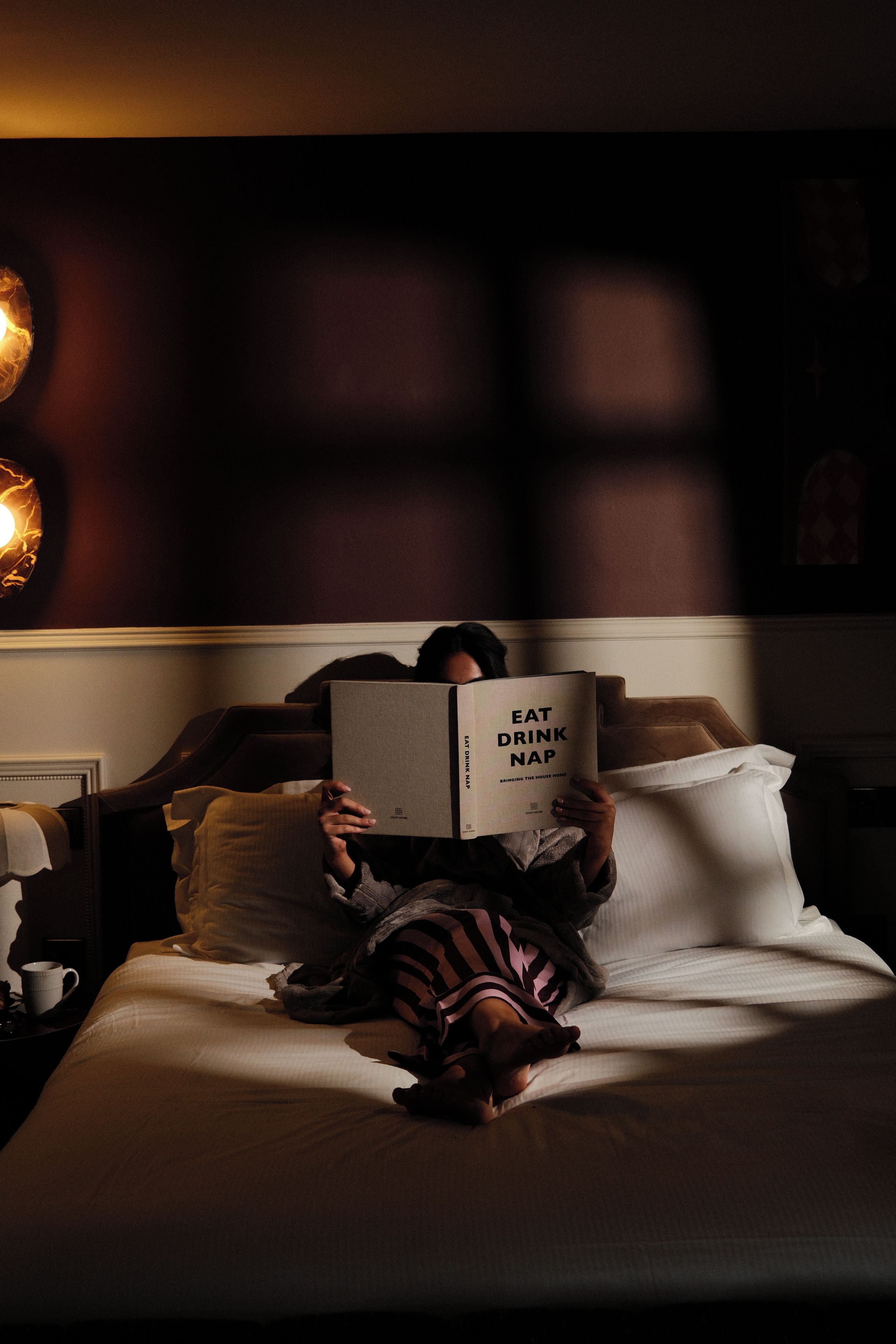 A person lying on a bed reading a book titled 'EAT DRINK NAP'.
