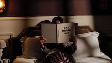 A person lying on a bed reading a book titled 'EAT DRINK NAP'.