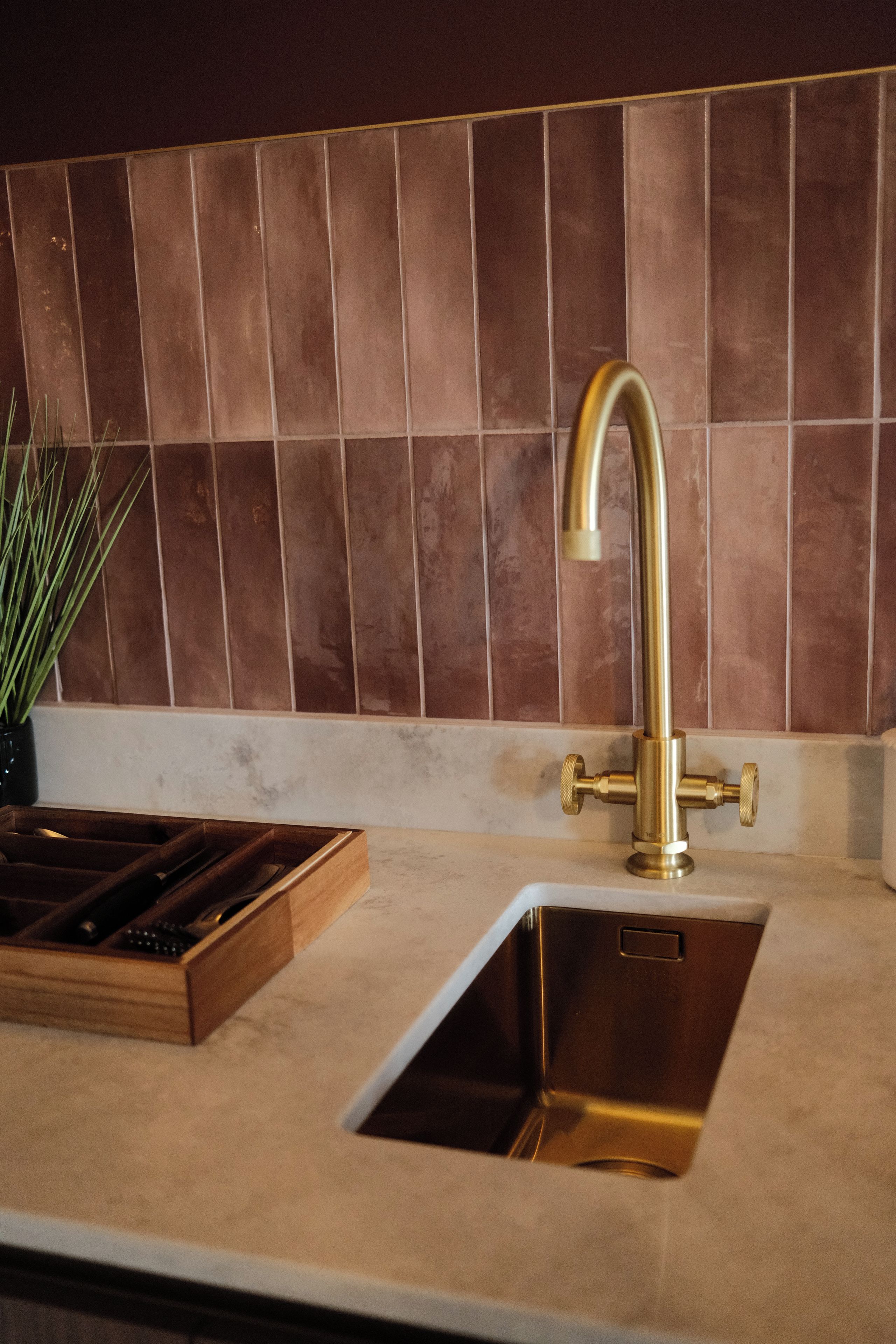 A kitchen with a stainless steel sink, a wooden tray, and a potted plant.