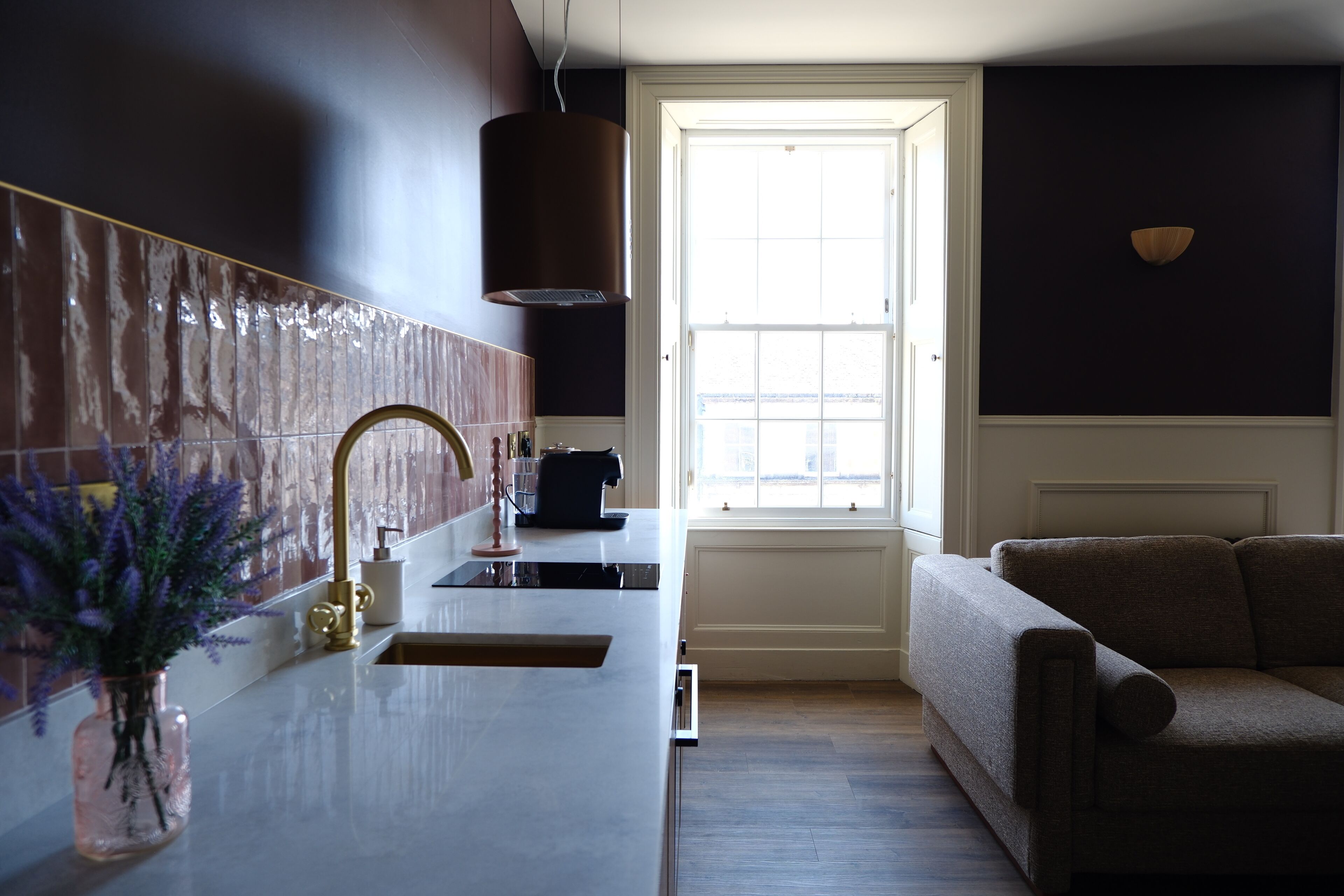 A modern kitchen with a white countertop, a gold faucet, and a window with a view.