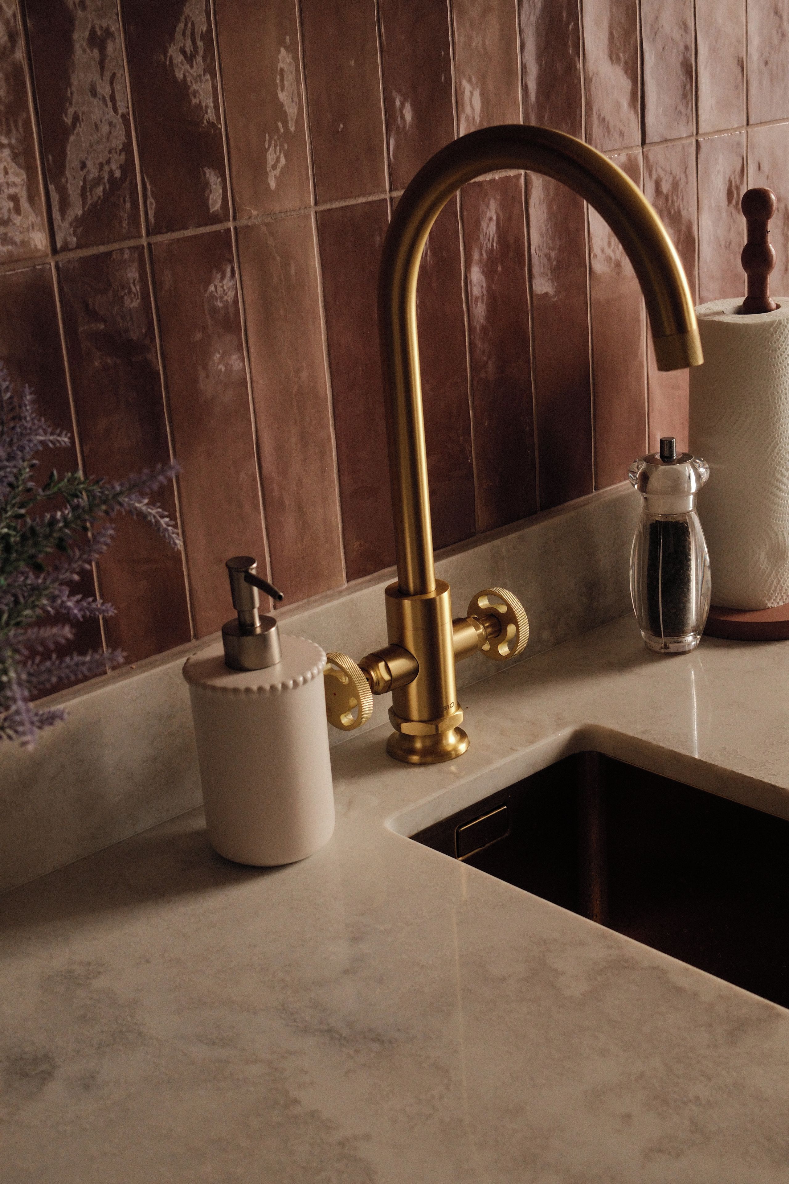 Eine Küche mit einem goldenen Wasserhahn, einem weißen Seifenspender und einem Glasbehälter mit Deckel.