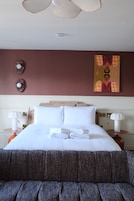 A hotel room with a large bed, two bedside tables, a painting on the wall, and a ceiling fan.